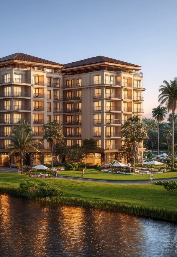 A modern mid-rise apartment building with balconies overlooks a landscaped lawn, palm trees, and a waterway at sunset, all expertly cared for by professional Commercial Property Maintenance Services.